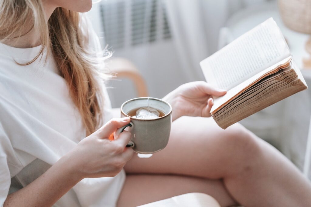 Woman reading a book with a hot cup of tea - just another way to treat yourself well. 