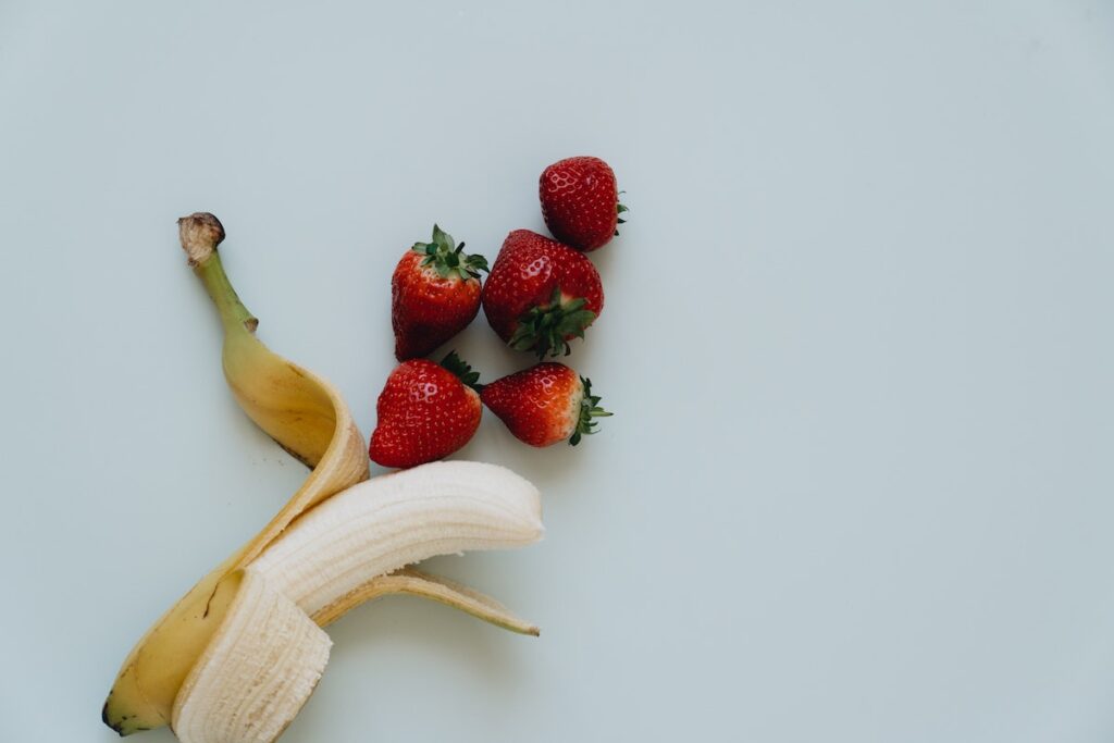 Unpeeled banana next to strawberries. 