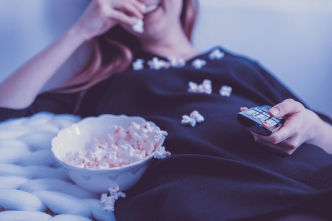 Woman laughing with popcorn on her lap while she binges TV. 