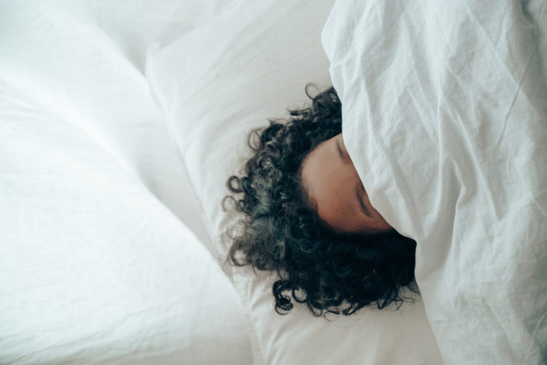 Woman sleeping underneath a comforter.