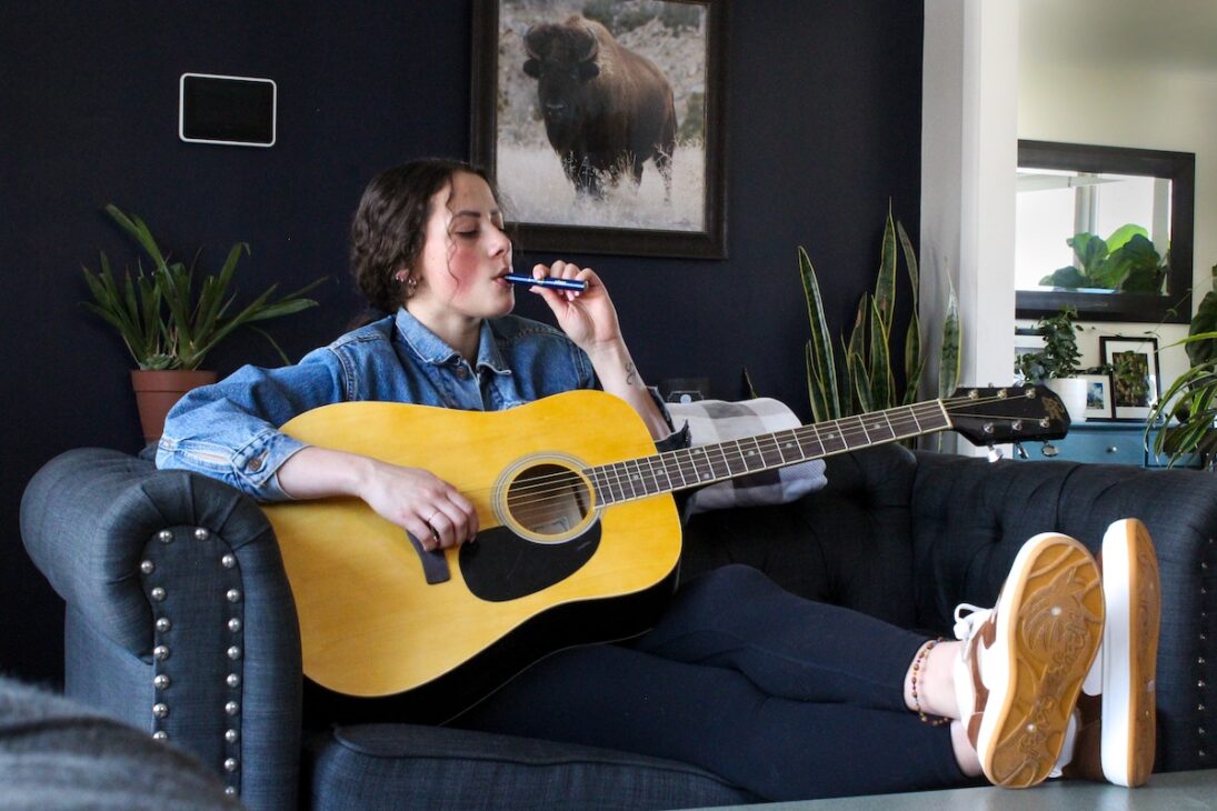 Woman vaping while playing the guitar.