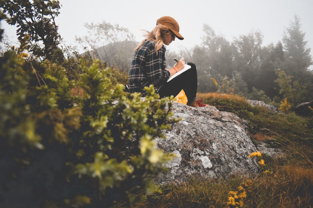 Woman on a rock writing in a journal 
