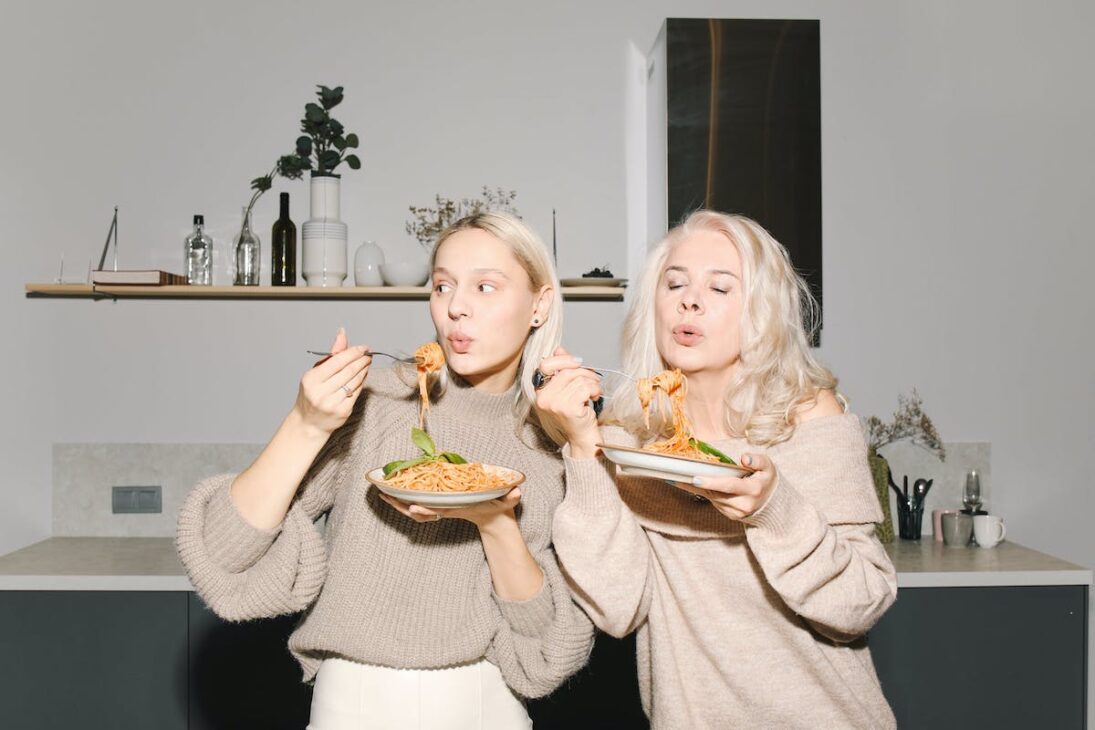 Two women eating pasta because they consumed appetite inducing cannabis mood gummies.